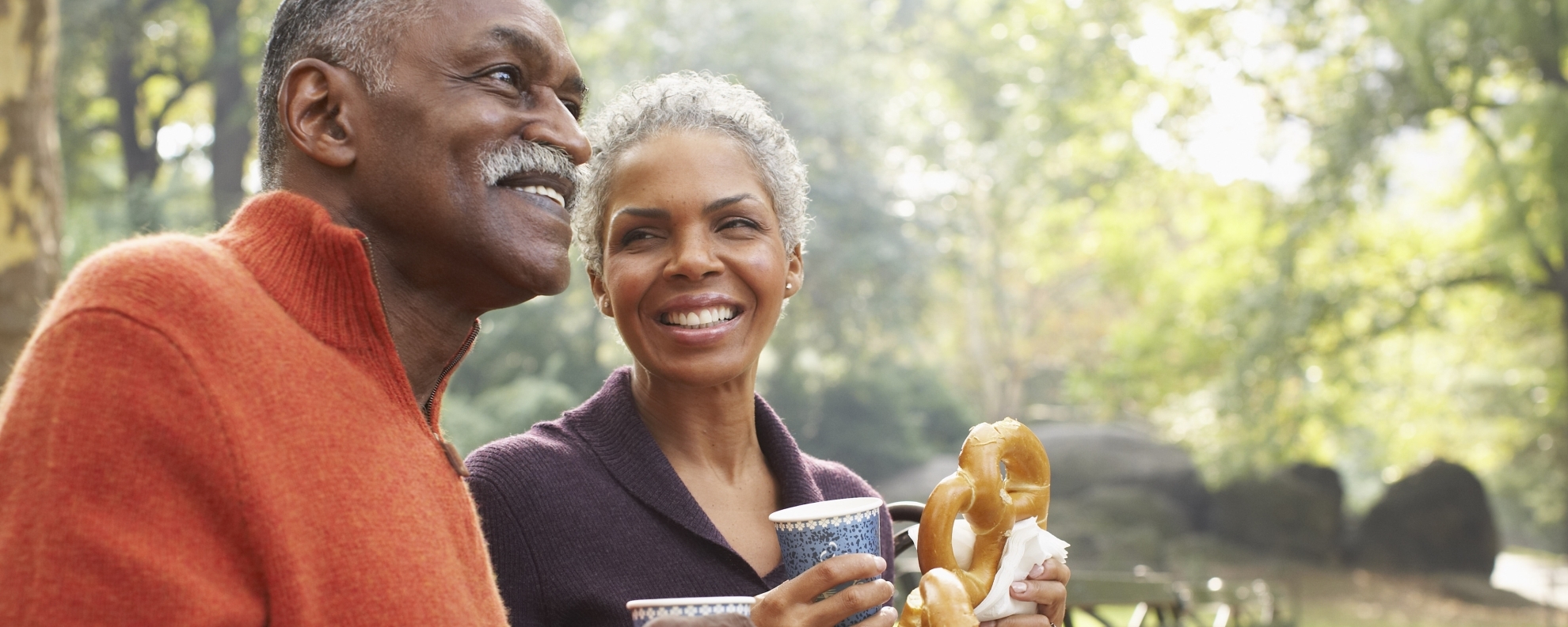 Senior couple eating pretzels on park bench